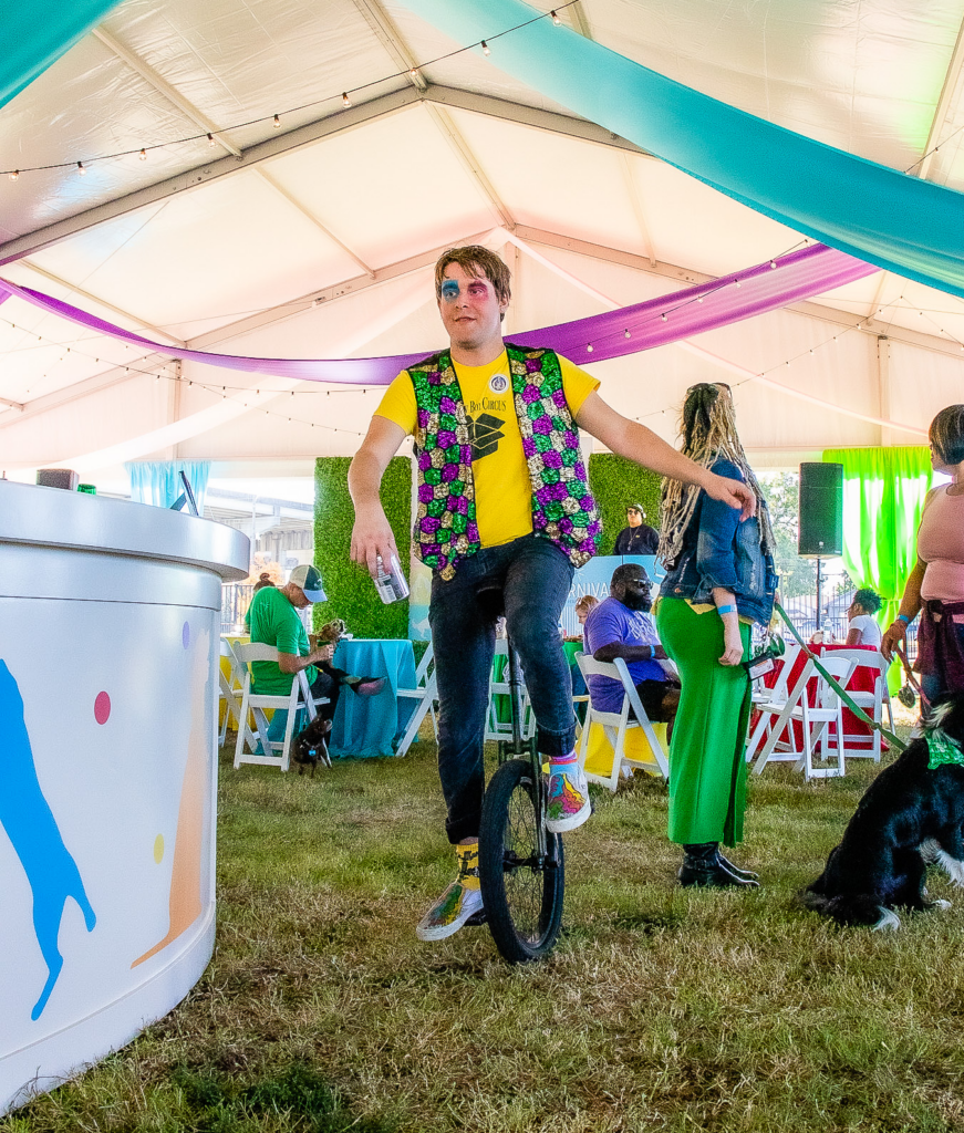 A yellow box circus member wearing a yellow shirt and vest rides a unicycle through the carnival